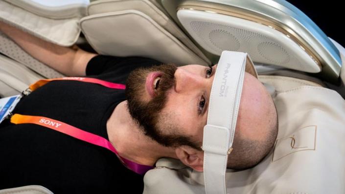 A man in a black shirt in a massage chair with his head held by a large strap.